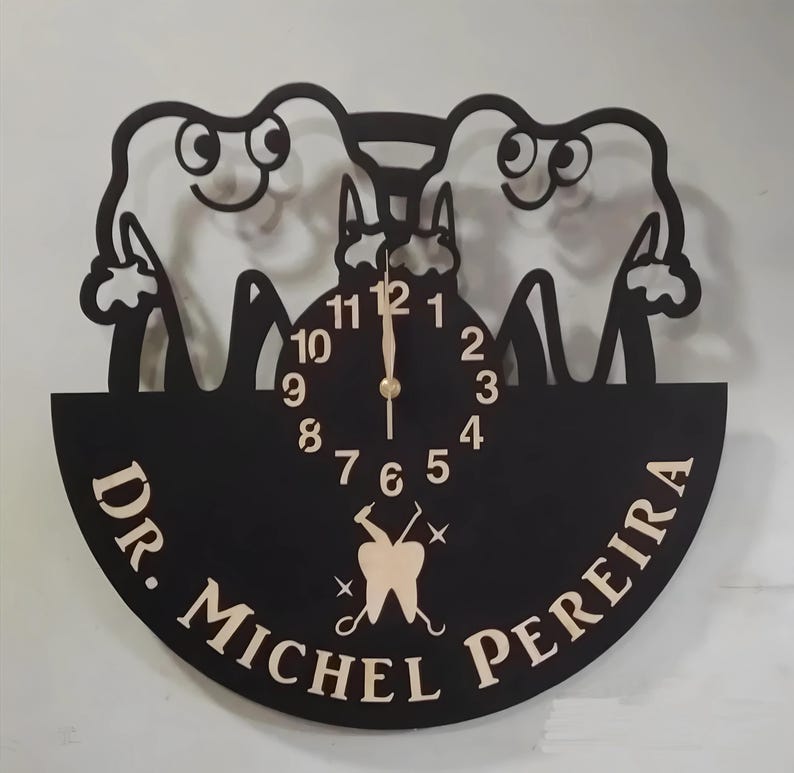 May include: Black and white clock with a dentist theme. The clock face is surrounded by two cartoon teeth with smiling faces. The clock face has gold numbers and hands. The clock is mounted on a black circular plaque with the text "Dr. Michel Pereira" in gold lettering.