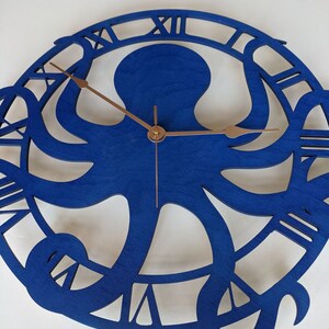 May include: A blue wooden wall clock with an octopus design. The clock face features Roman numerals and bronze hands. The octopus is the central design, with its tentacles forming the clock's frame.