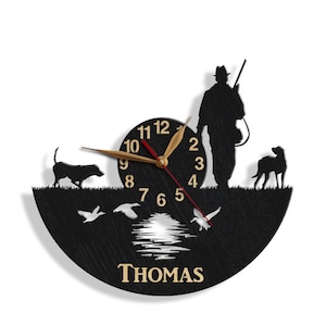 May include: Black silhouette wall clock with a hunter, two dogs, and ducks in flight. The clock face has Roman numerals and the name "THOMAS" is printed below the clock face.