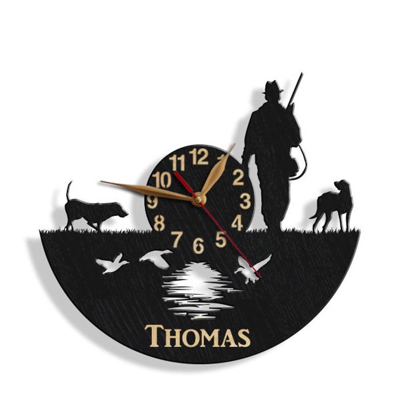 May include: Black silhouette wall clock with a hunter, two dogs, and ducks in flight. The clock face has Roman numerals and the name "THOMAS" is printed below the clock face.