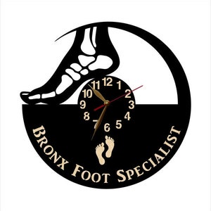 May include: A black and white wall clock with a foot skeleton design. The clock face is black with gold hands and numbers. The text "BRONX FOOT SPECIALIST" is printed on the bottom of the clock.