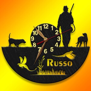 May include: Black wooden clock with a hunter, two dogs, and a pheasant design. The clock face has Roman numerals and the name "Russo" is written below the clock face.