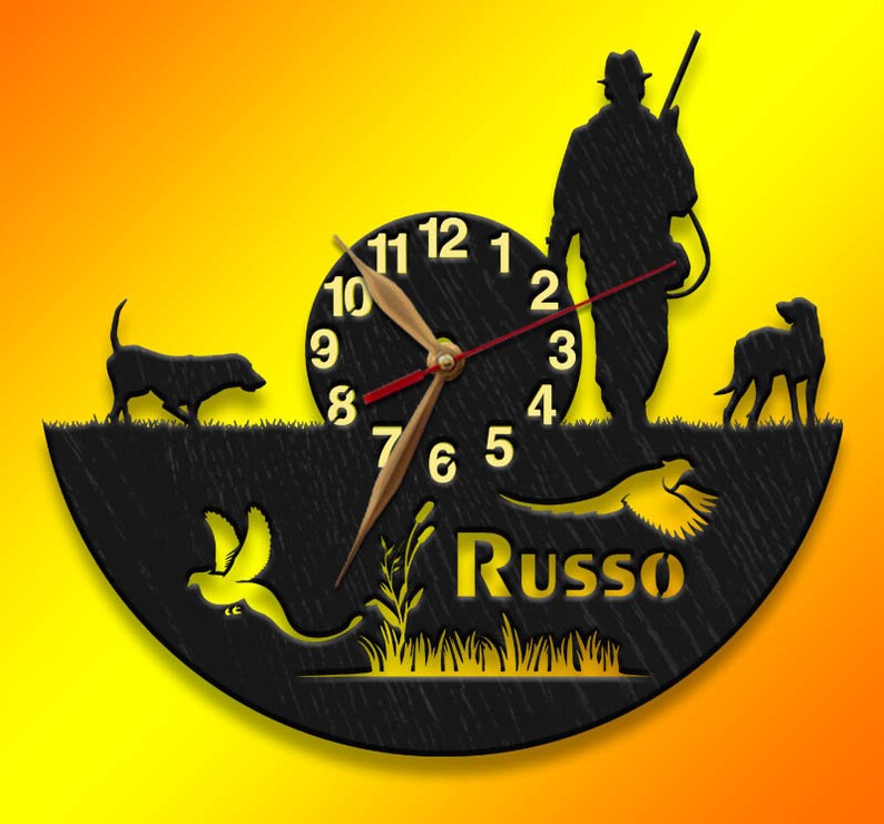 May include: Black wooden clock with a hunter, two dogs, and a pheasant design. The clock face has Roman numerals and the name "Russo" is written below the clock face.