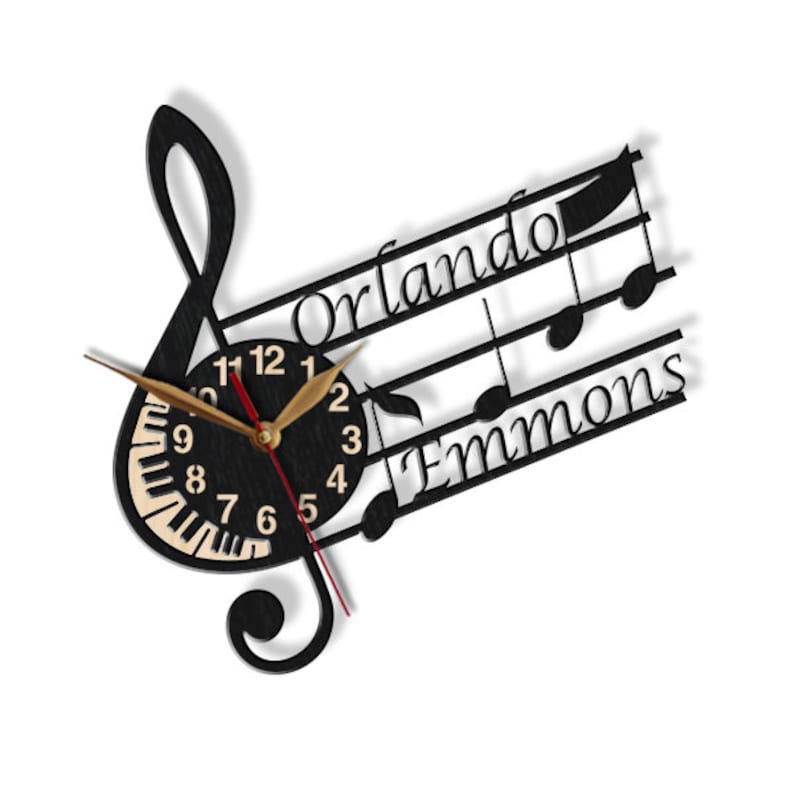 Puede incluir: Reloj de madera negro con un dise&ntilde;o de clave de sol. La esfera del reloj tiene un dise&ntilde;o de teclas de piano y los n&uacute;meros son dorados. El reloj est&aacute; personalizado con los nombres "Orlando Emmons".