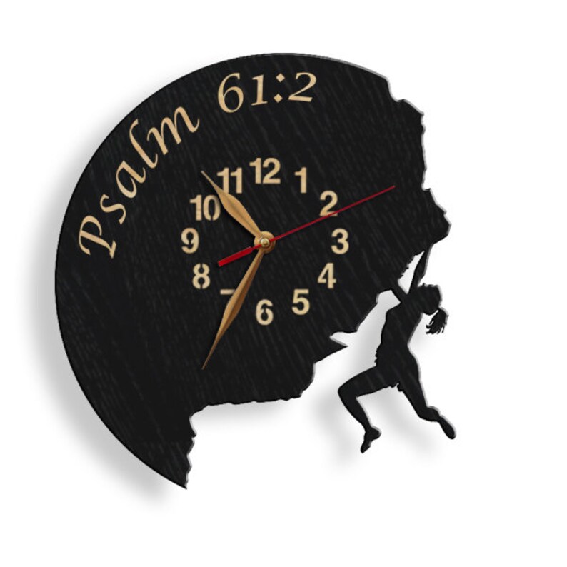 May include: Black wooden wall clock with a unique design. The clock face features the text "Psalm 61:2" and a silhouette of a person climbing a rock face. The clock hands are gold, and the second hand is red.