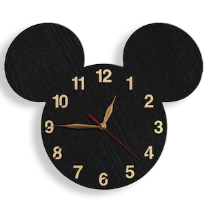 May include: Black wooden clock shaped like Mickey Mouse's head with gold numbers and hands. The clock face is black with gold numbers 1 through 12.