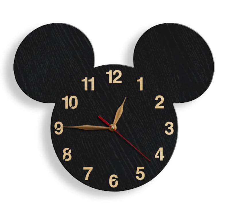 May include: Black wooden clock shaped like Mickey Mouse's head with gold numbers and hands. The clock face is black with gold numbers 1 through 12.