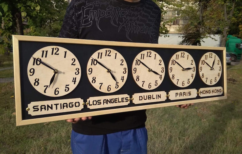 May include: A wooden world time zone clock with five clock faces. Each clock has a light-colored face with black numerals and hands. The clock displays the time in Santiago, Los Angeles, Dublin, Paris, and Hong Kong. The clock is framed in light wood.