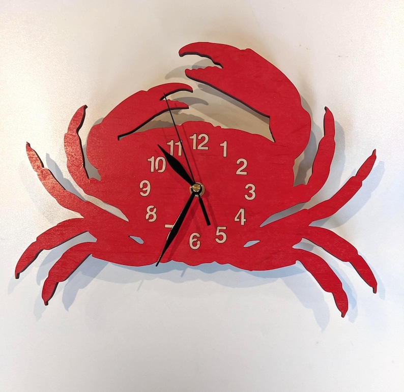May include: A bright red wall clock shaped like a crab. The clock face features light-colored numbers from 1 to 12 arranged in a circle on the crab's body. It has three black clock hands positioned at the center of the crab's shell.