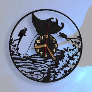 May include: Black wall clock with a silhouette of two scuba divers and a manta ray. The clock face has gold numbers and hands.