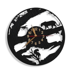 May include: Black wooden wall clock with a silhouette of two panthers and trees. The clock face has gold numbers and hands.