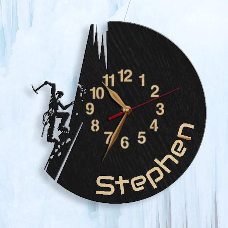 May include: Black wooden clock with a silhouette of a climber on a mountain. The clock face has gold numbers and hands. The name "Stephen" is written in gold letters at the bottom.
