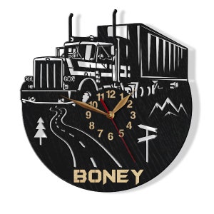 May include: Black wooden wall clock featuring a silhouette of a semi-truck, mountains, and a winding road. The clock face has gold numbers and hands. The name "BONEY" is written in gold letters below the clock face.