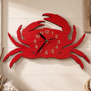 May include: A bright red wall clock shaped like a crab. The clock face is integrated into the crab's body and features black hour, minute, and second hands. The numbers one through twelve are printed in a light beige color on the red surface.