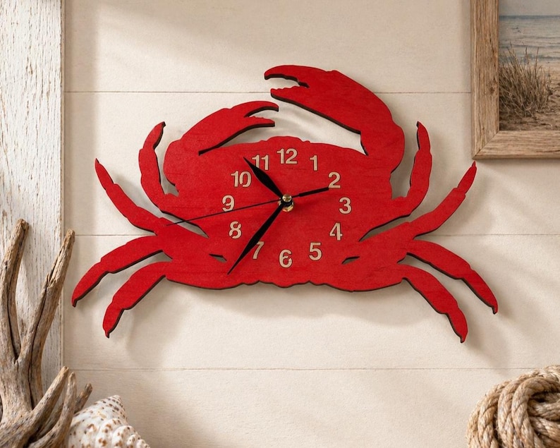 May include: A bright red wall clock shaped like a crab. The clock face is integrated into the crab's body and features black hour, minute, and second hands. The numbers one through twelve are printed in a light beige color on the red surface.