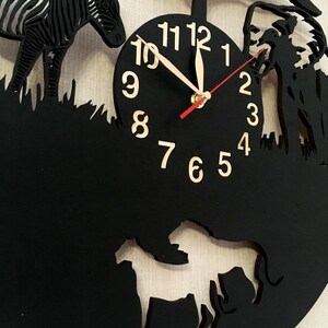 May include: Black clock with a white background and gold numbers. The clock face is surrounded by cutouts of a zebra, a lion, and a tree. The clock hands are red and white.