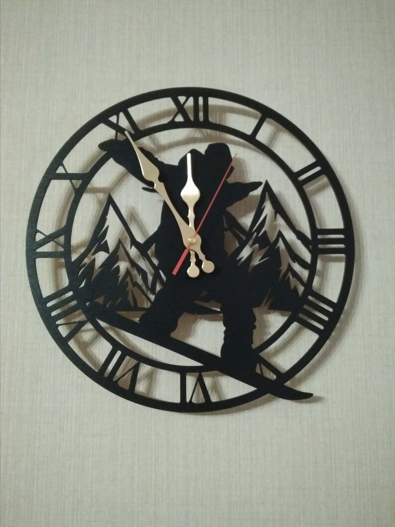 May include: Black metal wall clock featuring a silhouette of a snowboarder in a mountain scene. The clock face has Roman numeral markings.