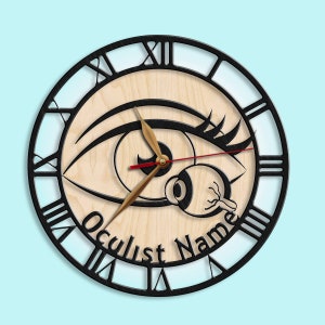 May include: A black and white clock with a large eye design. The clock face is made of wood and has Roman numerals. The clock hands are gold and red. The text "Oculist Name" is printed on the clock face.