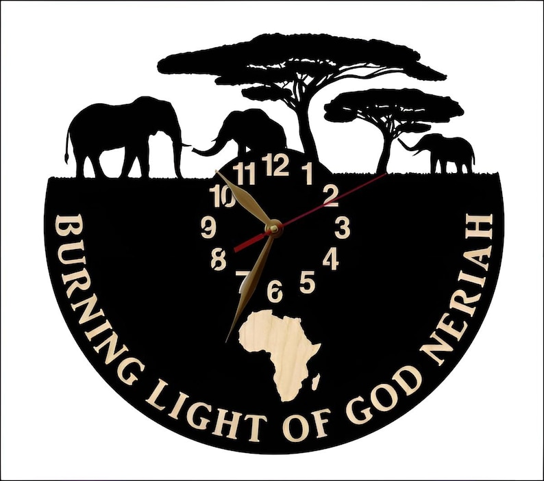 Puede incluir: Reloj de vinilo negro con una silueta de elefantes y &aacute;rboles. La esfera del reloj tiene una incrustaci&oacute;n de madera del continente africano. El texto "BURNING LIGHT OF GOD NERIAH" est&aacute; impreso alrededor de la esfera del reloj.