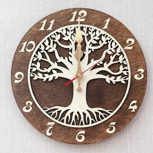 May include: A brown wooden clock with a white tree of life design. The clock face has Roman numerals and a red hour hand and a gold minute hand.