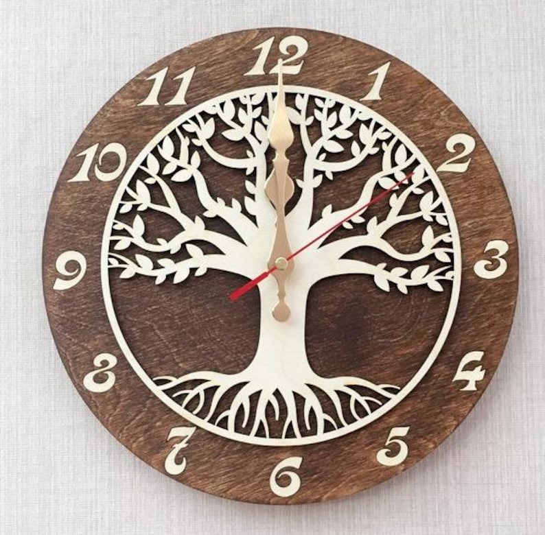 May include: A brown wooden clock with a white tree of life design. The clock face has Roman numerals and a red hour hand and a gold minute hand.