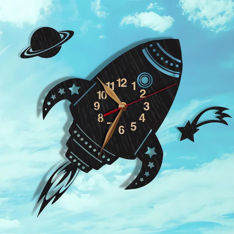 Puede incluir: Reloj de pared de madera negra en forma de cohete con manecillas doradas y una manecilla de segundos roja. La esfera del reloj tiene n&uacute;meros blancos y un c&iacute;rculo azul en el centro. El cohete tiene un dise&ntilde;o azul y blanco y una llama negra que sale de la parte posterior. Hay un planeta negro con un anillo alrededor y una estrella fugaz negra con una estrella blanca al final.