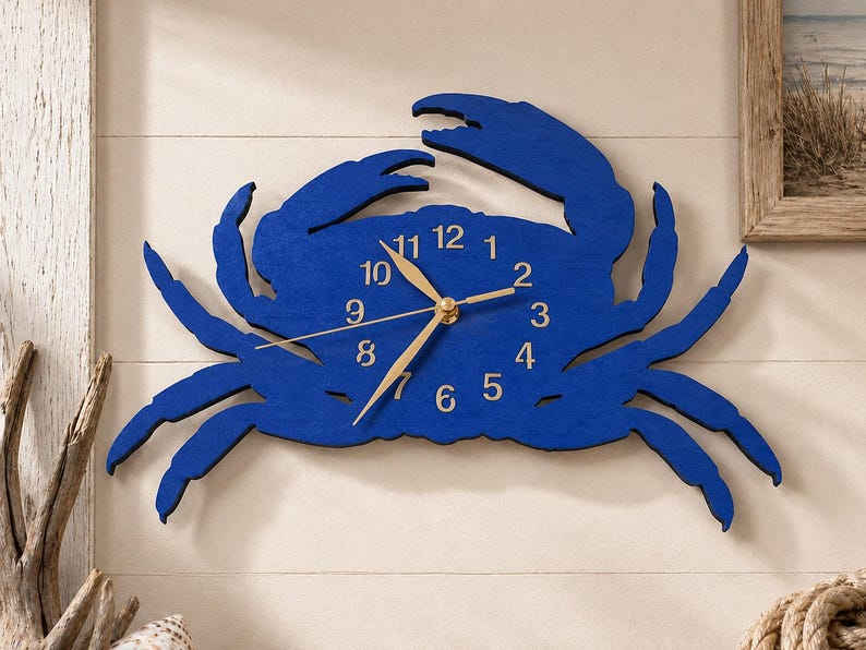 May include: A wall clock shaped like a crab with a deep blue finish. The clock face is integrated into the crab's body and features gold-colored numbers from 1 to 12, along with matching gold-colored hour, minute, and second hands at the center.