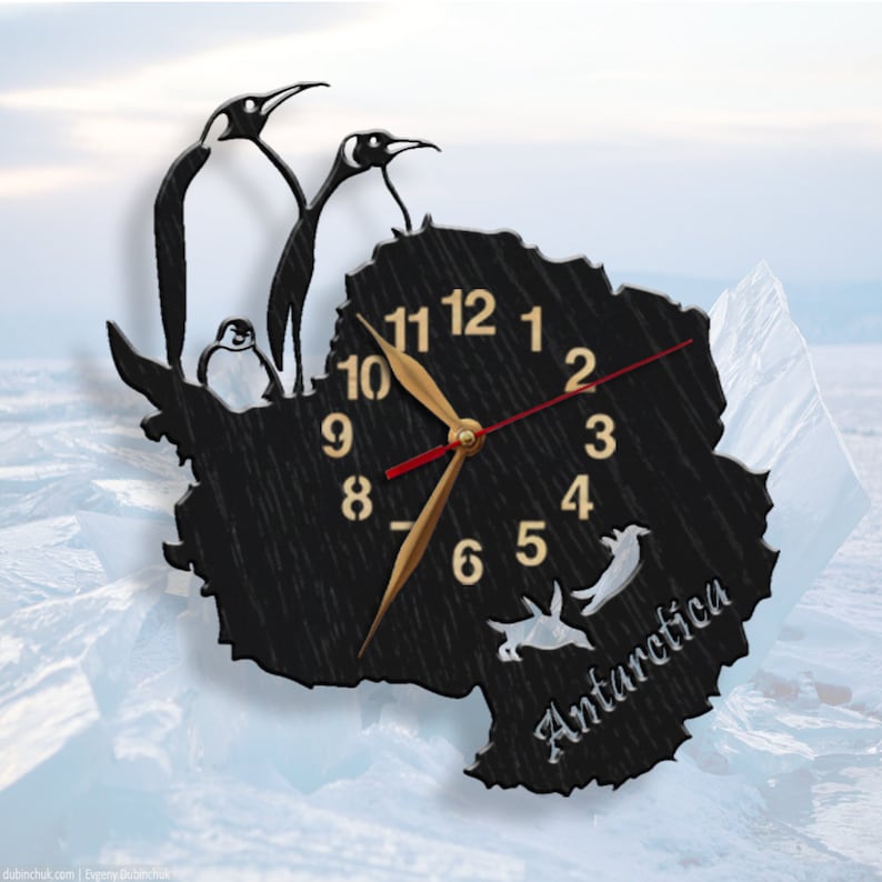 May include: A black wooden clock shaped like the continent of Antarctica with a gold clock face and black hands. The clock is surrounded by three penguins, two of which are standing on the top of the clock and one is sitting on the side. The clock face has the numbers 1 through 12 and the word "Antarctica" is written below the clock face.