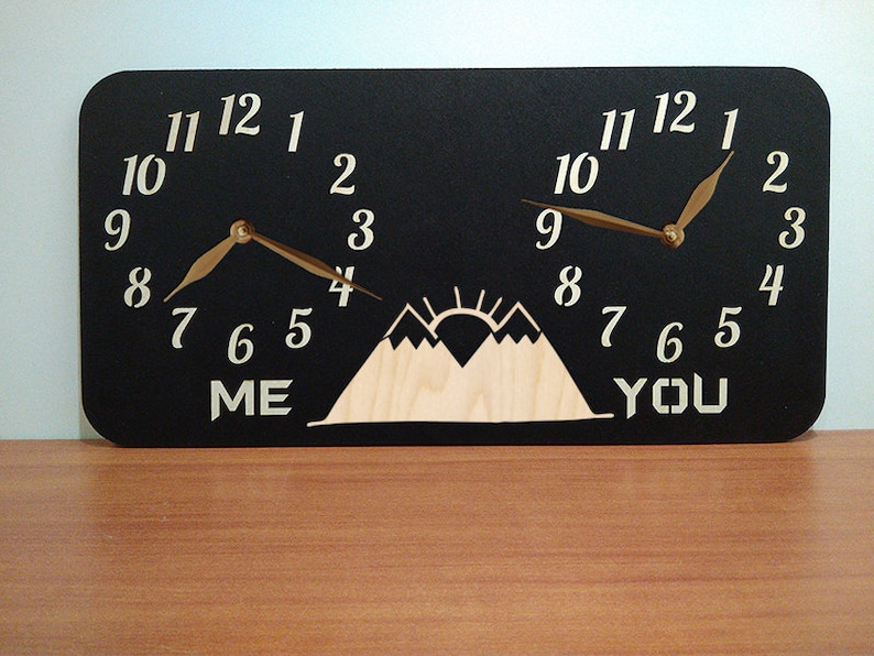 May include: A black wooden clock with two faces, each featuring a mountain silhouette and the words "ME" and "YOU" below. The clock hands are gold.