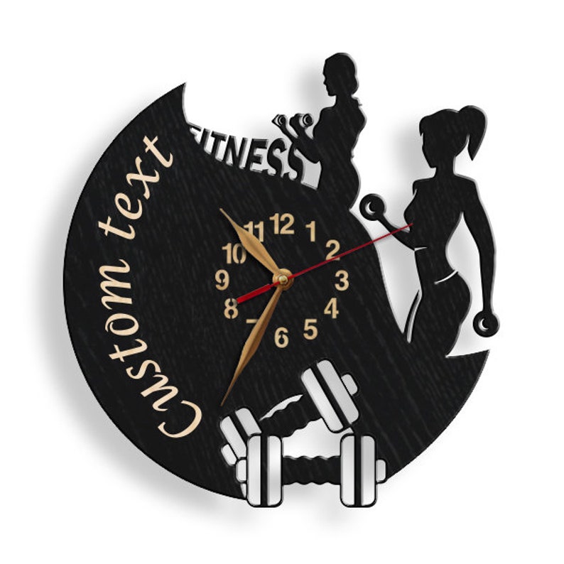 K&ouml;nnte beinhalten: Schwarze Holzuhr mit einer Silhouette von zwei Frauen, die Gewichte heben. Das Zifferblatt der Uhr hat goldene Zeiger und schwarze Zahlen. Der Text "Custom text" und "Fitness" ist auf der Uhr geschrieben.