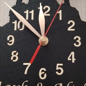 May include: A black wooden clock with white numbers and gold hands. The clock face is shaped like a silhouette of a couple. The clock has the text "Clark & Alish" at the bottom.