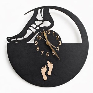 May include: A black wooden wall clock with a unique design. The clock features a cutout of a foot skeleton, a circular clock face with gold hands, and two small wooden footprints. The clock is mounted on a white background.