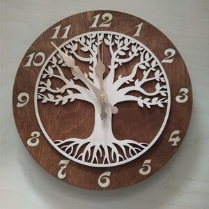May include: A brown wooden clock with a white tree of life design. The clock face has Roman numeral hour markers and a white background. The clock hands are gold.