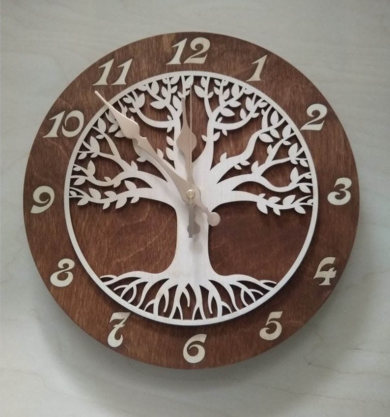 May include: A brown wooden clock with a white tree of life design. The clock face has Roman numeral hour markers and a white background. The clock hands are gold.