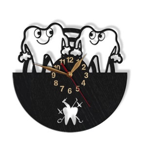 May include: A black and white wooden clock with a design of two cartoon teeth holding a toothbrush. The clock face has gold numbers and hands. The clock is shaped like a half circle and has a black background. The clock also has a small silver tooth with dental tools crossed behind it.