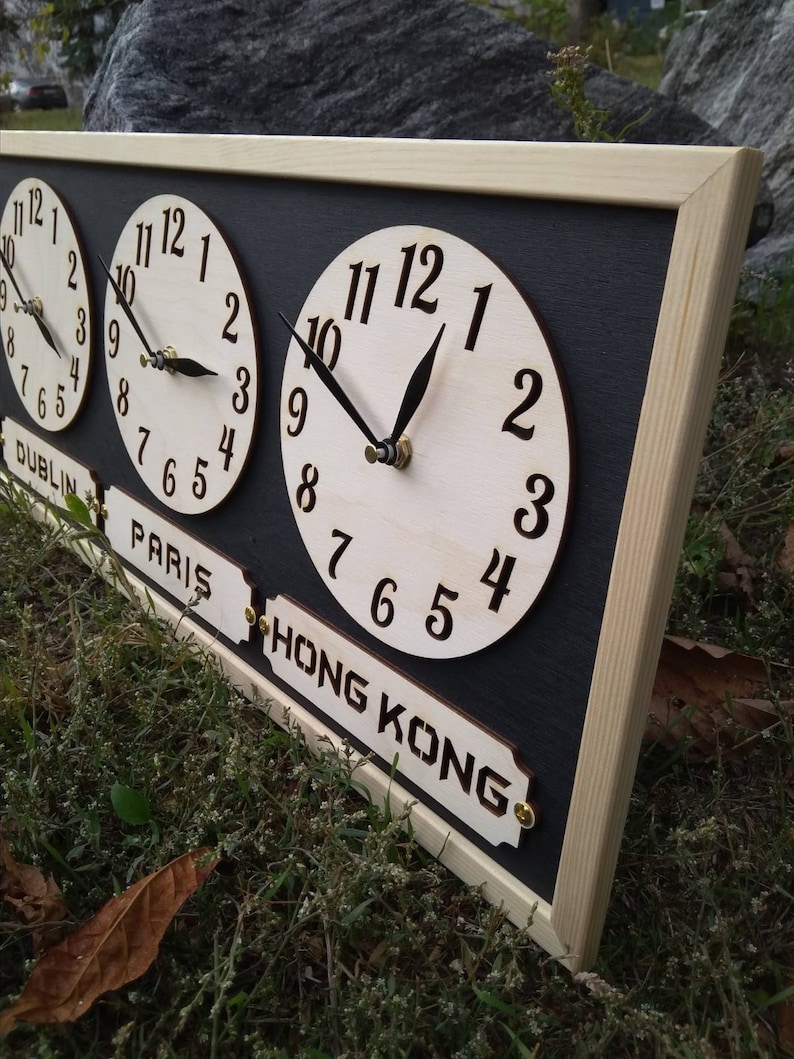 May include: A wooden world time zone clock with three circular clock faces. The clock has a black background, a light wood frame, and labels for Dublin, Paris, and Hong Kong. The clock hands are black.