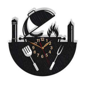 May include: Black and white wall clock with a grill, spatula, and fork design. The clock face has a black background with white numbers and hands.