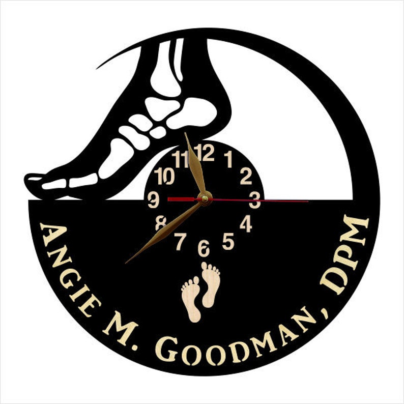 May include: A black and white wall clock featuring a foot skeleton silhouette above a clock face. The clock hands are gold. The clock face has the numbers 1-12. The words "ANGIE M. GOODMAN, DPM" are printed on the clock.