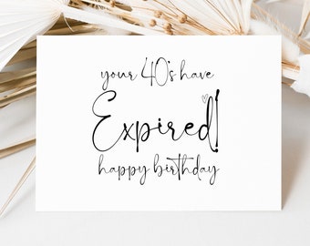 May include: White card with black text that reads "your 40's have expired! happy birthday". The card is sitting on a white surface with dried palm leaves.