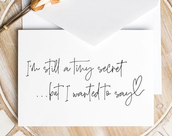 May include: A white card with black calligraphy that reads "I'm still a tiny secret... but I wanted to say."  The card is on a wooden tray with a decorative pattern.