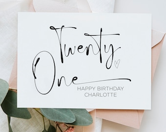 Puede incluir: Una tarjeta blanca con caligrafía negra que dice "Twenty One" con un pequeño símbolo de corazón. El texto "Happy Birthday Charlotte" está impreso debajo de la caligrafía.
