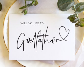 May include: A white card with black text that reads "Will you be my Godfather?" with a small heart drawn next to the text. The card is on a white plate with a gold rim.