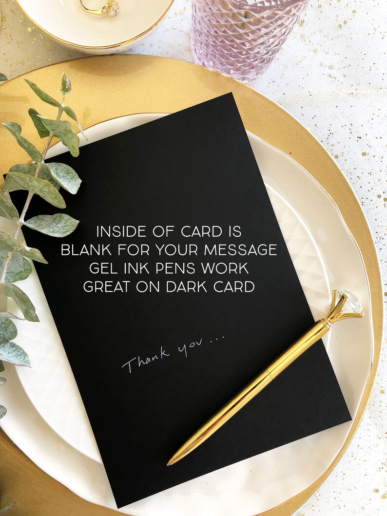Puede incluir: Una tarjeta negra con texto blanco que dice "INSIDE OF CARD IS BLANK FOR YOUR MESSAGE GEL INK PENS WORK GREAT ON DARK CARD" y "Thank you..." escrito con tinta blanca. Un bol&iacute;grafo dorado con una parte superior en forma de diamante est&aacute; sobre la tarjeta.