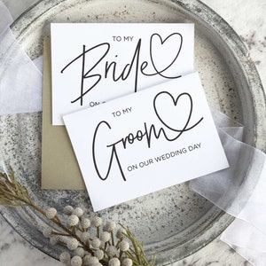 May include: Two white cards with black calligraphy. The top card says "To My Bride" with a heart. The bottom card says "To My Groom" with a heart and "On Our Wedding Day".