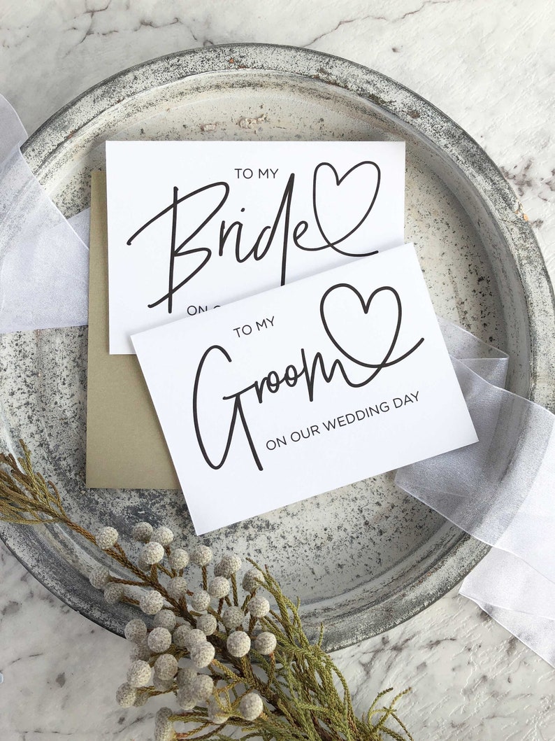 May include: Two white cards with black calligraphy. The top card says "To My Bride" with a heart. The bottom card says "To My Groom" with a heart and "On Our Wedding Day".