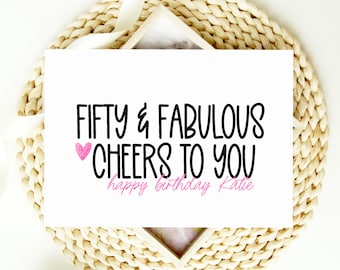 Puede incluir: Una tarjeta blanca con texto negro que dice "Fifty & Fabulous Cheers to You" con un corazón rosa y las palabras "happy birthday Katie" en rosa.