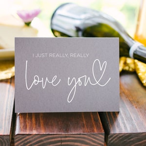 Może przedstawiać: Szara kartka z tekstem "I just really, really love you" napisanym białym, ozdobnym pismem z sercem narysowanym obok słowa "you".