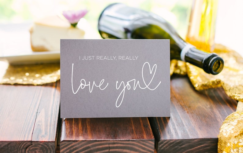 Może przedstawiać: Szara kartka z tekstem "I just really, really love you" napisanym białym, ozdobnym pismem z sercem narysowanym obok słowa "you".