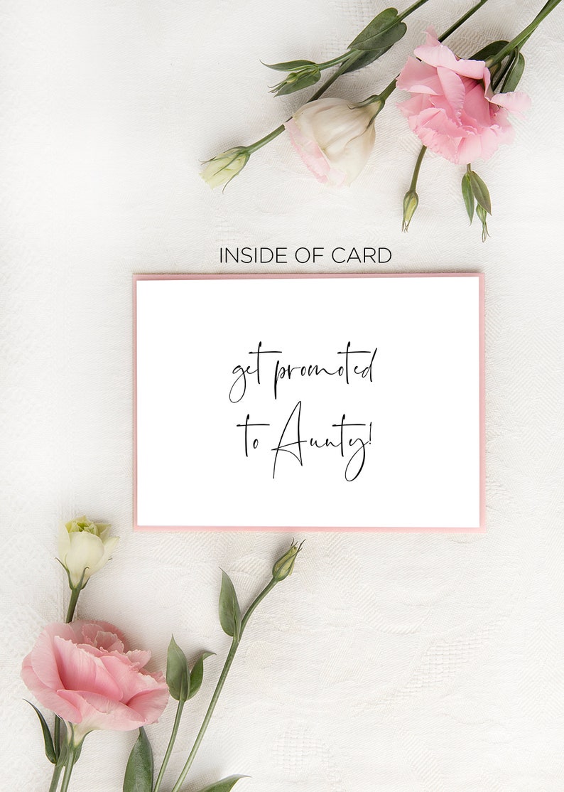 May include: A white card with pink trim and the text "get promoted to Aunty!" written in black cursive. The card is surrounded by pink and white flowers.