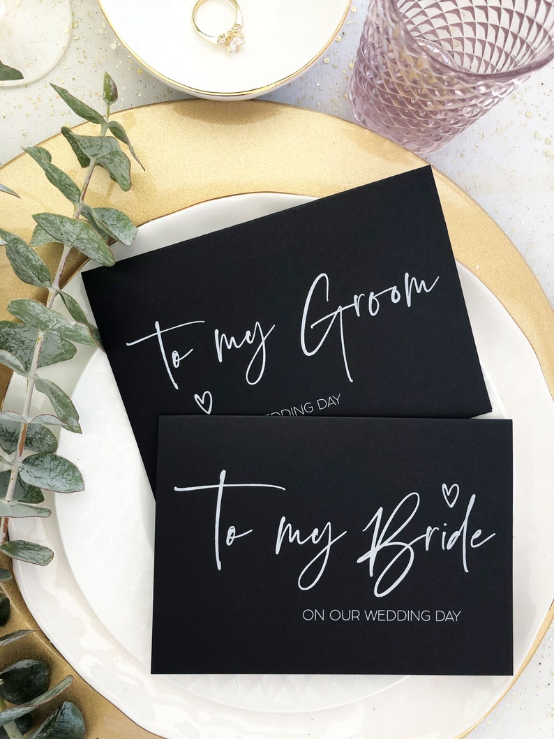 Pode incluir: Dois cart&otilde;es pretos com letras brancas. O cart&atilde;o superior diz "To my Groom" com um pequeno s&iacute;mbolo de cora&ccedil;&atilde;o e o texto "Wedding Day". O cart&atilde;o inferior diz "To my Bride" com um pequeno s&iacute;mbolo de cora&ccedil;&atilde;o e o texto "On our Wedding Day".